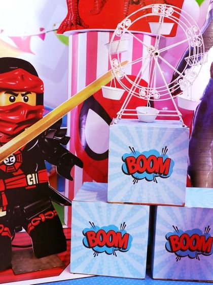 A close-up of the fun props at the Superhero Carnival party, including a LEGO Ninjago character and "BOOM" comic book style blocks.