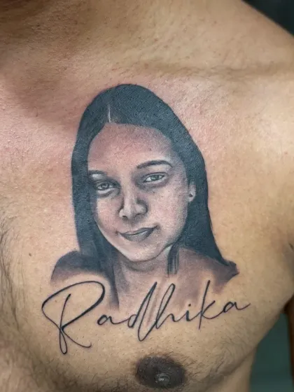 A chest tattoo combining a realistic portrait with a custom script name, "Radhika". This is a beautiful way to honor a loved one, placing their image and name over the heart.