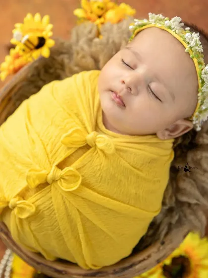 A peaceful newborn girl in a yellow wrap, looking like a little sunflower herself. The colors are warm and inviting, reflecting the joy of a new arrival.