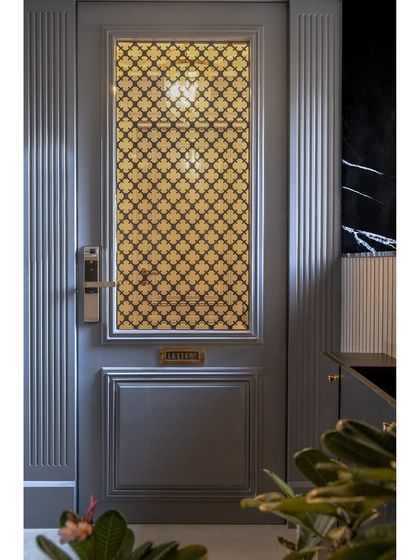 This elegant main door features a classic design with fluted paneling and a decorative gold-tone grille. It's a timeless choice that adds a touch of grandeur and sophistication to the home's entrance.
