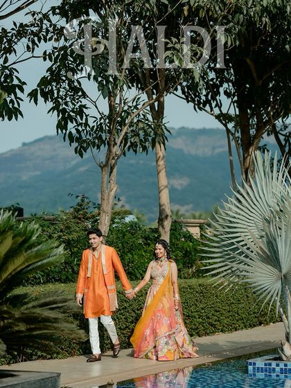 A cinematic shot of the couple taking a walk by the pool at their Haldi venue in Lonavala, with the mountains in the background.