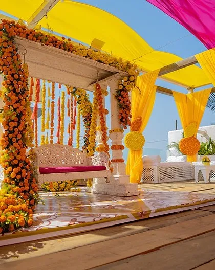 A classic Haldi setup, featuring a beautiful swing decorated with marigolds and a canopy of vibrant yellow and pink drapes. It's traditional, bright, and full of joy.