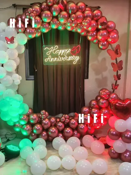 A romantic first-anniversary decoration for a home. The setup includes a heart-shaped balloon arch in metallic red and white, a neon sign, and a light-up number '1'.
