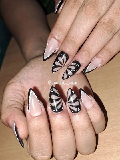A dramatic set of long stiletto nails. The design features a sharp V-french with reflective glitter and accent nails with a bold butterfly wing pattern.