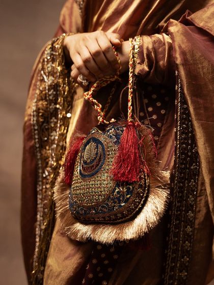 A detailed shot of a traditional 'potli' bag, showcasing the intricate embroidery and tassels. This image focuses on the accessories that complete a classic Indian look, perfect for a couture campaign.