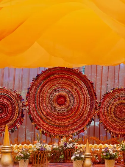 The stage backdrop for the equestrian Haldi, featuring large, circular woven mats in shades of red and orange, creating a rustic and textural focal point.