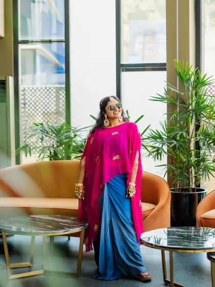 For the bride's Haldi, we chose this unique and modern outfit. A bright pink embroidered cape is layered over a draped blue skirt, creating a bold and stylish look that stands out.