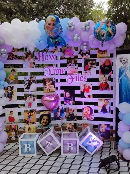 A 'How Time Flies' photo memory wall for a Frozen-themed party, decorated with pastel balloons and character cutouts.
