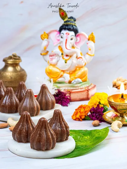 Chocolate modaks styled with a Ganesha idol for the festival. The clean, white marble background gives a modern and pure feel to this traditional sweet.