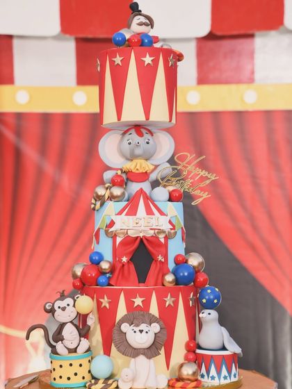 An incredible, tall carnival-themed cake, featuring multiple tiers decorated with circus animals like an elephant, monkey, and sea lion.