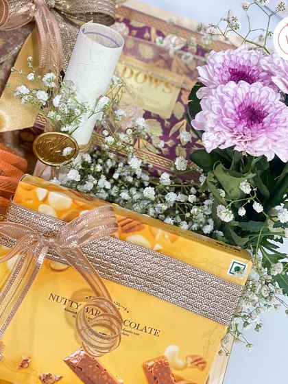 This close-up shows the details within the wooden tray hamper. You can see the hand-rolled invitation scroll, sealed with a custom wax seal, nestled beside nutty chocolate bars and fresh flowers.