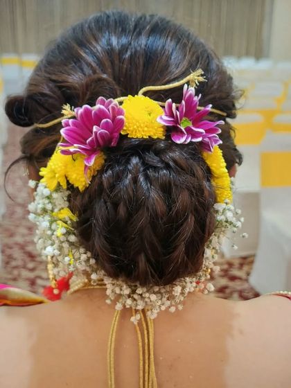 A detailed look at the intricate braided bun. This hairstyle is a masterpiece of texture and form, beautifully decorated with fresh, colorful flowers.