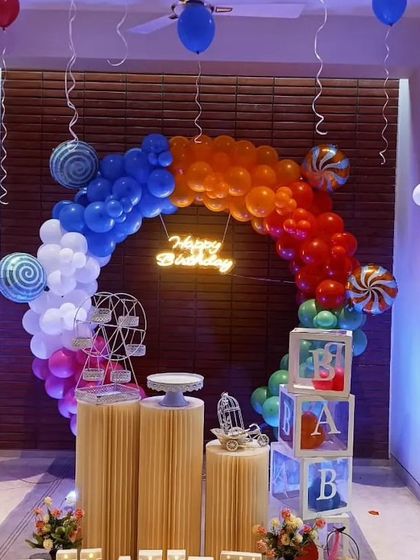 A vibrant and colorful setup ideal for a baby's first birthday or a toddler's party. It includes a rainbow balloon arch, light-up 'BABY' blocks, and decorative elements like a mini Ferris wheel.