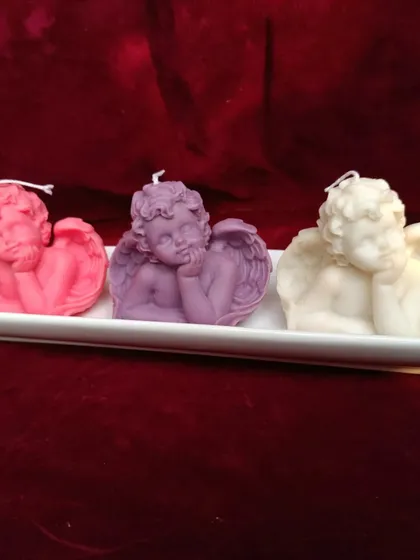A set of three cherub or angel-shaped candles in pink, purple, and white.