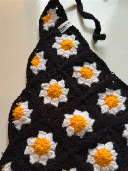 A closer look at the daisy granny square pattern on the black crochet bandana. Each little flower is stitched with care.