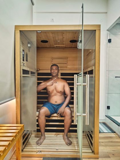 A client gives a thumbs-up from inside our spacious infrared sauna cabin. The full-glass door and comfortable seating are designed to make your session feel open and relaxing, never claustrophobic.