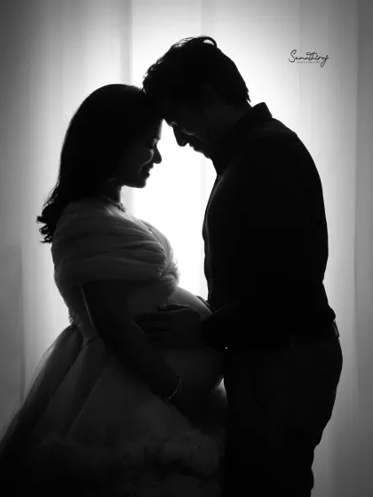 A classic backlit silhouette of a couple against a bright window. The dramatic contrast highlights their forms and the intimate moment they share, creating a timeless black and white image.