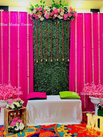 The main seating area for the Mehendi/Dholki night, with a pink and green backdrop, a comfortable diwan, and cherry blossom floral arrangements.