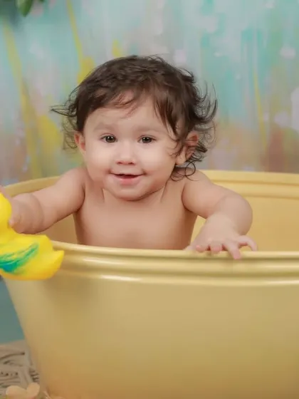 This happy baby plays with a rubber duck during his bath time session. We use classic, fun props to encourage natural smiles and playful interactions.