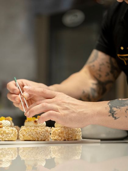 A chef carefully placing a garnish with tweezers. Our masterclasses focus on the fine details that elevate a dessert from good to great.
