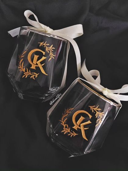 Personalized elegance for a newlywed couple. These geometric glasses are engraved with a custom 'CK' monogram surrounded by a laurel wreath, a classic design symbolizing victory and honor.