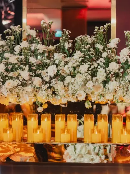 A beautiful arrangement of white flowers and candles on a reflective gold base, adding a touch of luxury and warmth to the decor.