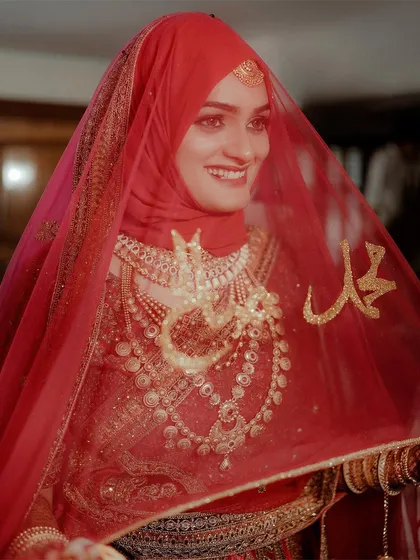 The details of a bride's attire tell a story of heritage and love. Here, the rich red of the veil and the intricate gold jewelry frame her radiant smile, creating a portrait that is full of warmth and tradition.