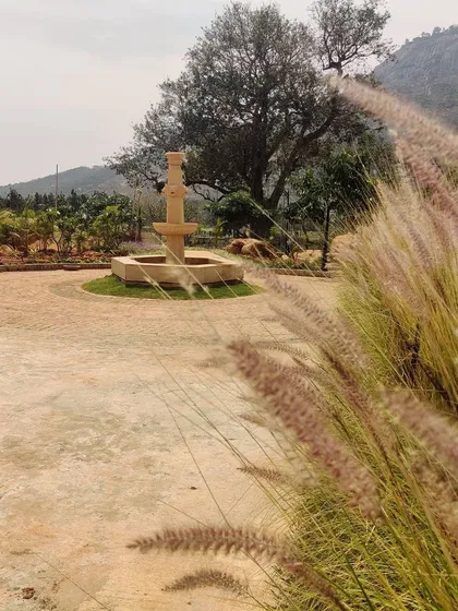 A classic stone fountain serves as a focal point in this garden driveway. The soft, feathery grasses in the foreground contrast with the hardscape, demonstrating our use of texture and form in landscape design.