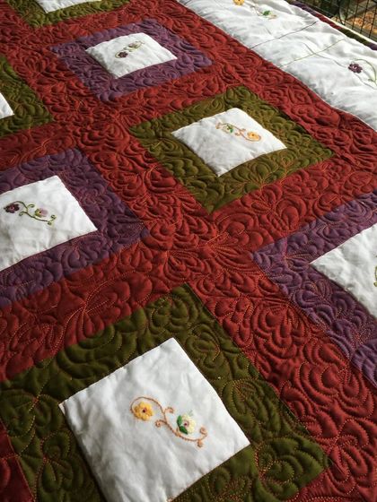 A close-up of a quilt with embroidered flowers, surrounded by dense, custom free-motion quilting.