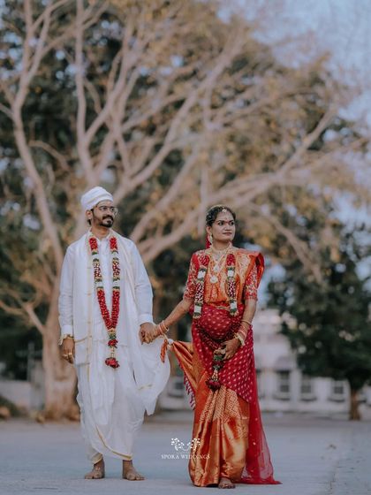The couple holding hands, the bride's red saree and the groom's white dhoti creating a classic and beautiful contrast.