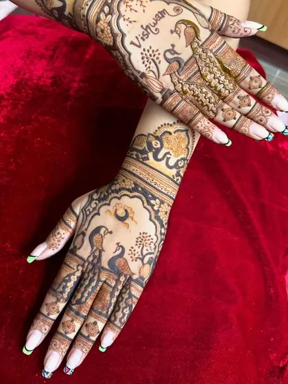 Graceful peacocks are the centerpiece of this design, surrounded by delicate foliage and the groom's name hidden within the art. The elephant on the wrist adds a royal touch.