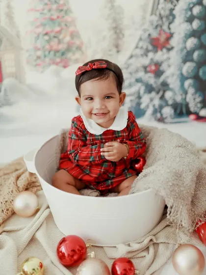 A perfect Christmas smile! This little girl looks absolutely adorable in her plaid dress, sitting in a bucket surrounded by festive ornaments.