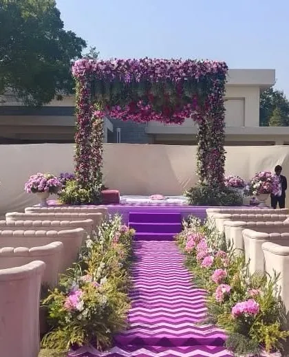 A beautiful mandap and aisle setup for a purple-themed day wedding. The aisle is lined with flowers and leads to a stunning mandap covered in purple and pink floral arrangements.