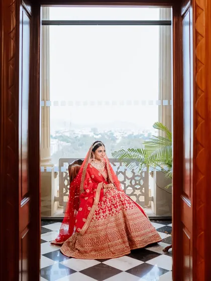 A classic bridal portrait, with the bride seated in a doorway, the light catching her red lehenga perfectly.