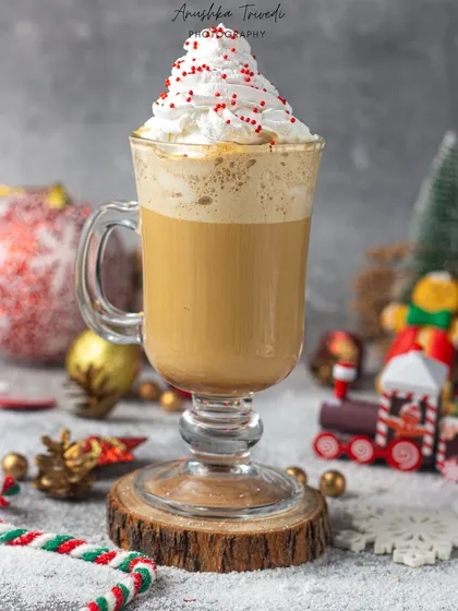 A festive Christmas coffee topped with whipped cream and sprinkles. The holiday-themed props in the background create a warm and cheerful seasonal atmosphere.