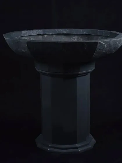 A large, bowl-shaped pedestal planter in a dark stone finish. It's a grand and imposing piece, suitable for large plants or floral arrangements.