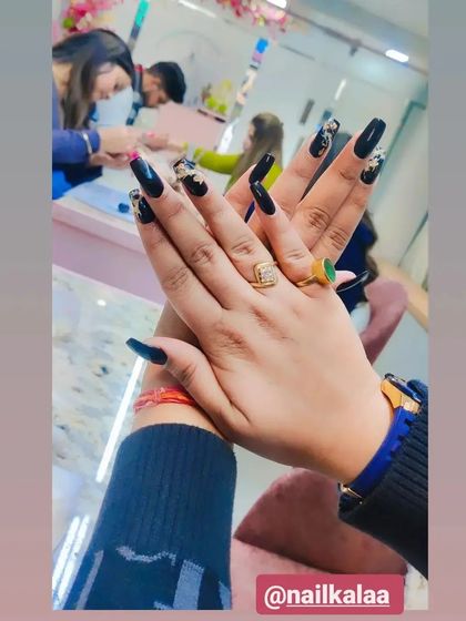 A bold and dramatic set of long, black coffin nails with gold and white abstract accent art.