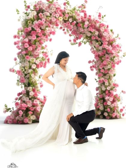 A truly romantic portrait of the dad-to-be kneeling before his partner under a stunning pink and white floral arch. This grand setup creates a fairytale-like moment.