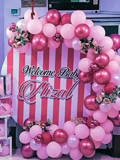 A stylish "Welcome Baby" backdrop in pink and white stripes, framed by a beautiful arch of pink and chrome-pink balloons.