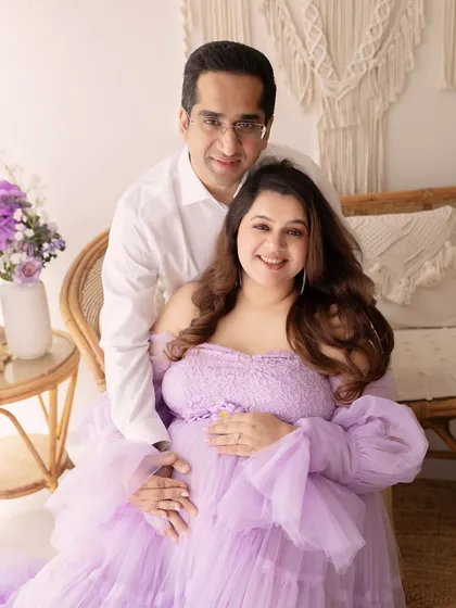 A serene portrait of an expecting couple. The soft lavender dress and boho-chic studio setup create a dreamy and romantic atmosphere.