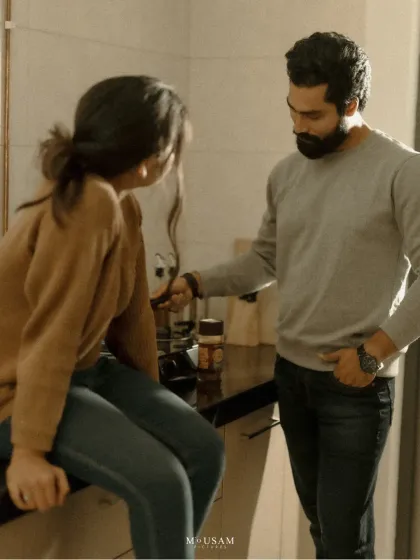 A playful, candid moment during their at-home shoot. He points to something, making her laugh as she sits on the kitchen counter. It’s these unscripted interactions that reveal the true nature of a couple's bond.