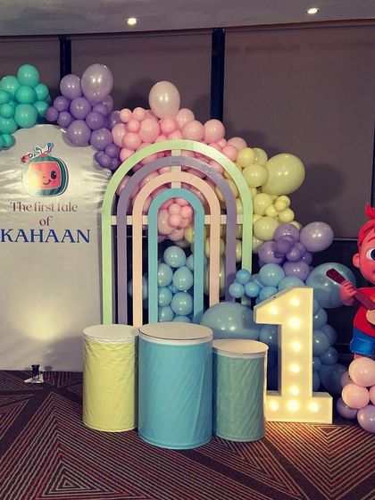 A pastel-colored Cocomelon theme for a first birthday, featuring a JJ cutout, a light-up number '1', and rainbow-themed arch backdrops.
