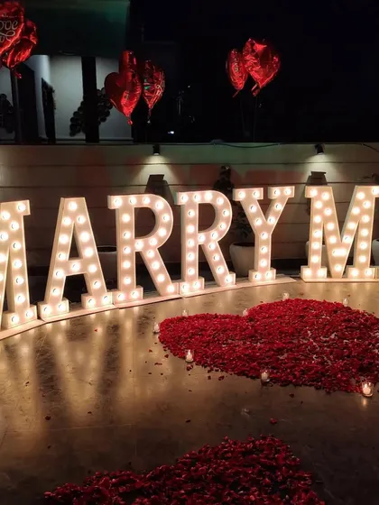 Another angle of our terrace proposal setup, showing the glowing marquee letters and heart-shaped arrangements of red rose petals. Red foil heart balloons add a final romantic touch to the scene.