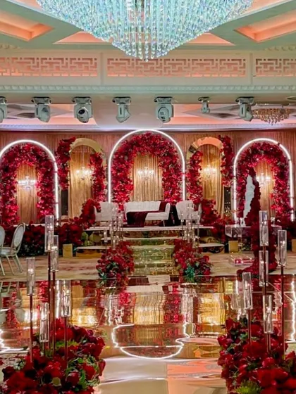 An opulent reception stage with a mirrored floor, multiple red floral arches, and crystal chandeliers, showcasing a truly luxurious decor theme.