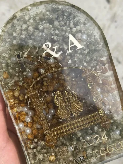 A different view of the arch-shaped keepsake, showing how the silver initials and date complement the golden kaleera inside.
