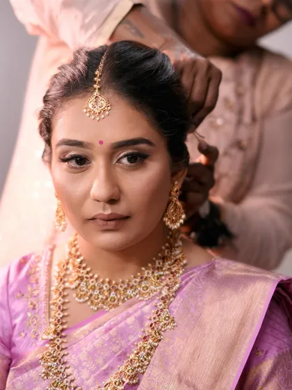 A portrait of the bride as her hair is being styled. Her makeup is complete, showcasing a beautiful winged liner and glowing skin.