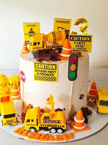 A construction zone-themed cake for a 3rd birthday, complete with toy trucks, traffic cones, and "caution" signs. It's a playful design for a child who loves big vehicles.