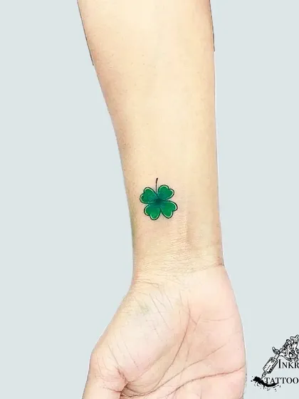 A bright green four-leaf clover on the wrist. This small color tattoo is a classic symbol of good luck.
