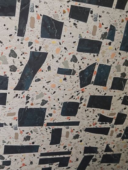 A close-up of a modern terrazzo-style tile. The irregular, colorful chips embedded in the surface create a playful and contemporary look.