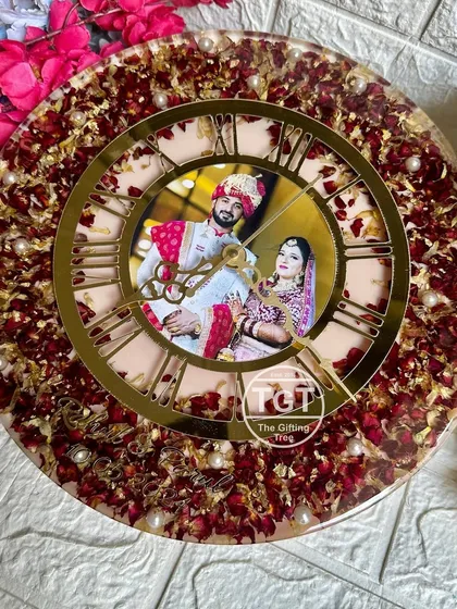 This 12-inch round clock features a unique design where the wedding photo is placed directly in the center, framed by a golden Roman numeral dial. The outer ring is filled with preserved red rose petals from the varmala.
